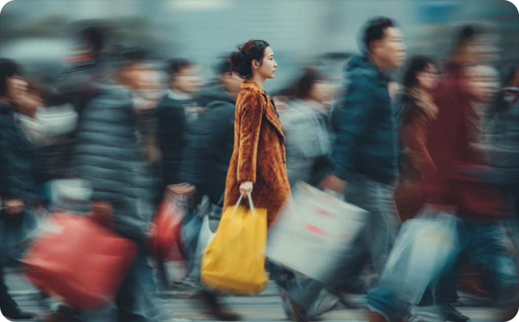 A girl with a yellow bag and in a brown coat walks in a crowd on the street