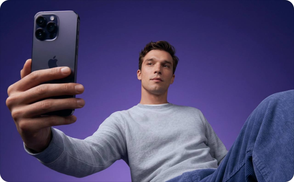 Male model in a studio with a purple background holding a smartphone toward the camera, demonstrating a UGC video style versus AI UGC content in a modern tech ad setup