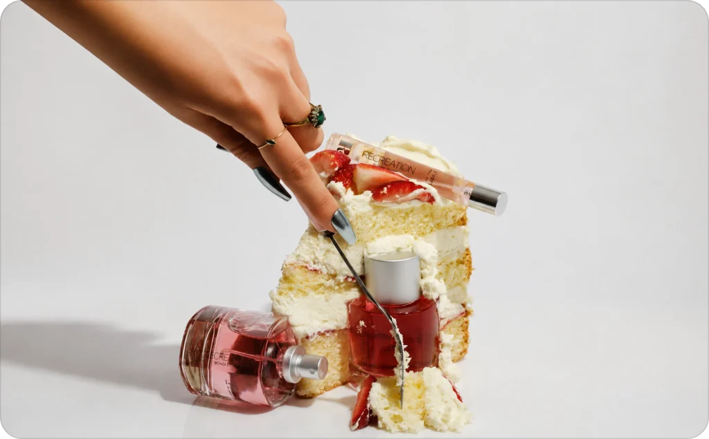 A hand slices a strawberry cream cake surrounded by perfume bottles, showcasing creative AI product placement.